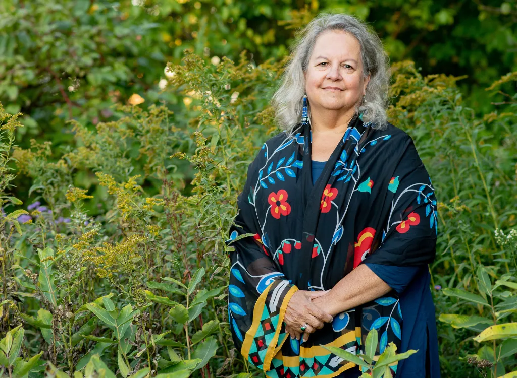 Portrait photo of Robin Wall Kimmerer standing in a field of goldenrod and aster.