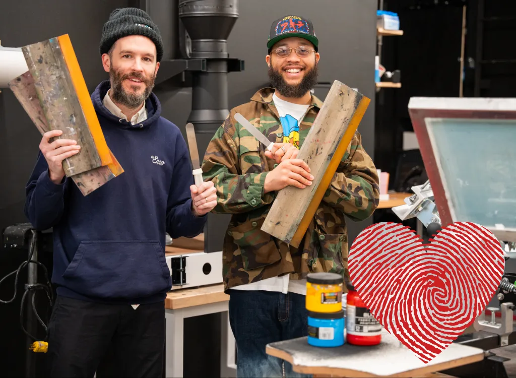 Artists Dan Crane and Paris Gaines stand holding screen printing equipment.