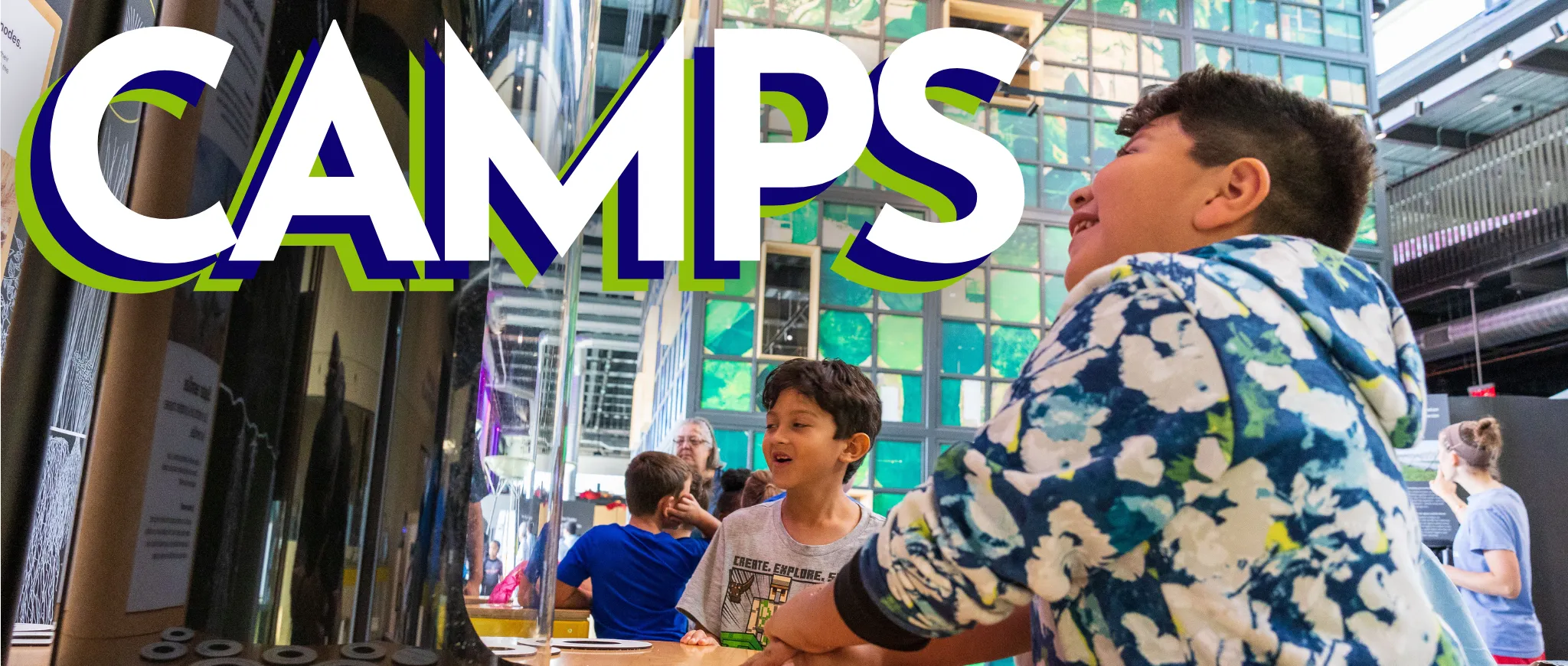 Two young students smile while engaging with a Luminarium exhibit. Text overlay reads: Camps